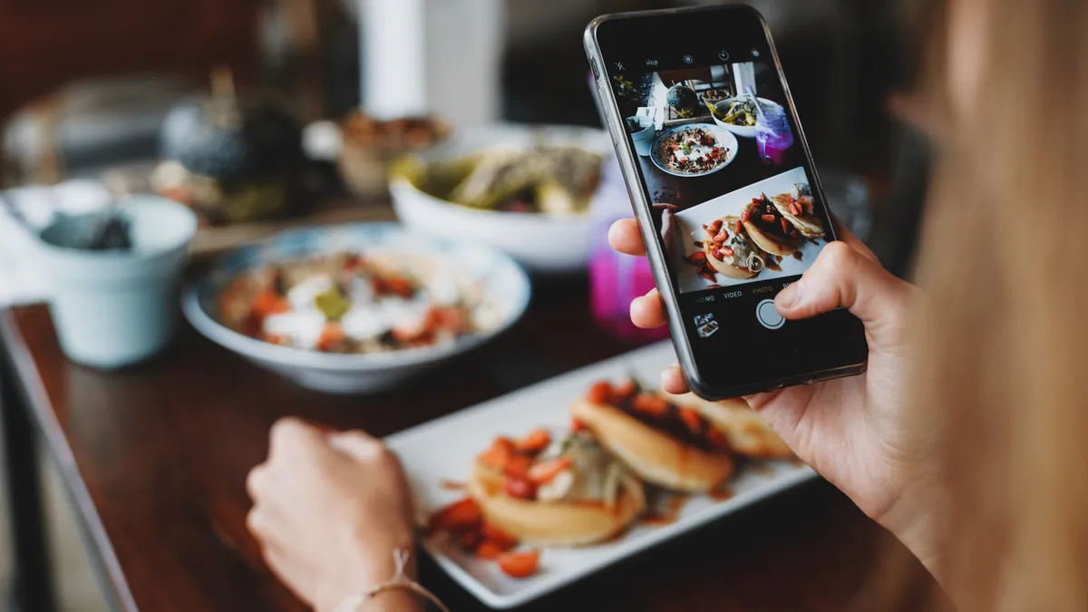Une cliente photographie ses plats avec son téléphone, à une table de restaurant.