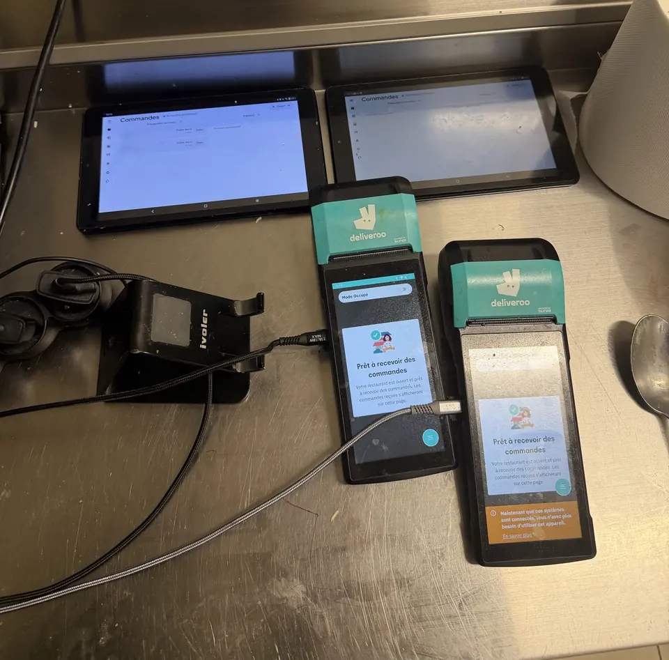 Deux tablettes de commandes et deux terminaux Deliveroo côte à côte sur le plan de travail d’une cuisine